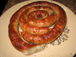 Homemade sausage baked in oven,
made from beef and chicken meat
and pieces of lard. Smoked meat appetizer
on a plate on table. Photos of food for holiday.