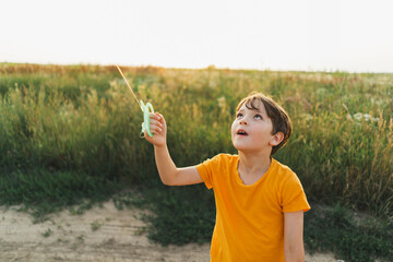 Candid Portraits. Portrait of a boy in nature. A boy in an orange T-shirt flies a kite in nature. Happy child, lifestyle.