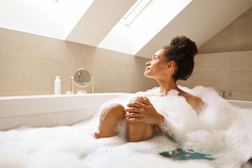 Woman relaxing in bathtub full of foam in bathroom of house
