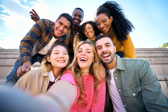 Group of multiethnic friends taking selfie with smart mobile phone outdoors. Happy young multiracial people smiling together looking at camera. University students having fun in college campus