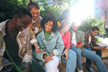Diverse group of university friends sitting on stairs in street city. Happy students using and looking smartphones while smiling thrilled and excited. Chatting and commenting fun things in mobiles. - obrazy, fototapety, plakaty