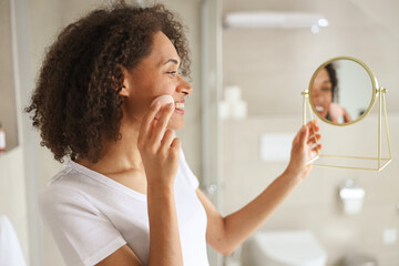 A woman in towel smiles while looking at her reflection in the bathroom mirror