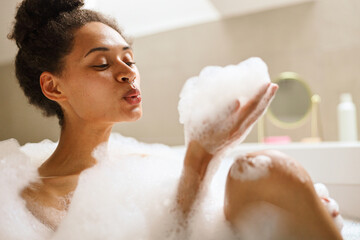 A happy woman bathing in a foamy spa tub, gesturing artfully with eyelashes