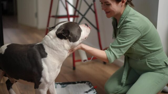Slow motion. A pregnant woman sitting on the floor on her knees plays with a dog with a paint roller and kisses the dog on the nose. The woman smiles and pets the dog