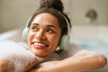 Woman, happy in a bathtub, smiling with black hair and headphones
