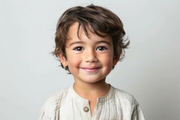 A young boy with brown hair and a white shirt is smiling