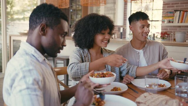 Group of multi-racial friends sitting around table enjoying meal at dinner party together - shot in slow motion 