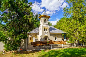 A small church with a steeple sits in a wooded area - obrazy, fototapety, plakaty