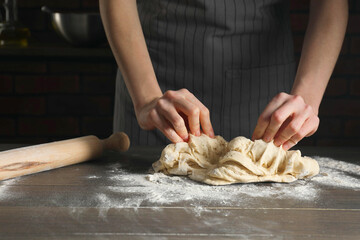 Making bread. Woman kneading dough at wooden table in kitchen, closeup
