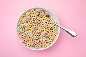 Tasty cereal rings in bowl and spoon on pink table, top view