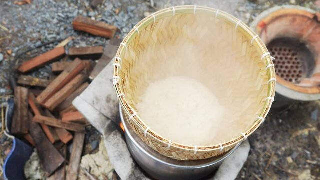 Sticky rice cooked in wicker bamboo steamer with laos aluminum steel pot on the charcoal stove in the agricultural garden house area.