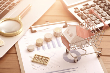 Office supplies and coins on data drawings, as well as small houses placed in shopping carts