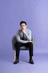 Portrait of Asian business man sitting on sofa, isolated on purple background