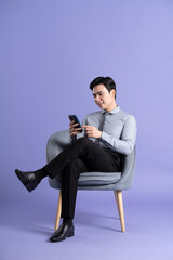 Portrait of Asian business man sitting on sofa, isolated on purple background