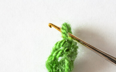 Close-up view of metal crochet hook and green wool thread on white background. Top view of hook for needlework and crocheting. DIY concept. Macro, flat lay, copy space, mock up