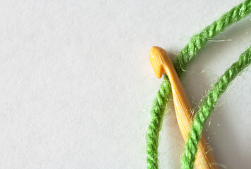 Close-up of wooden crochet hook and green wool thread on white background. Top view of hook for needlework and crocheting. DIY concept. Empty space for text. Macro, flat lay, copy space, mock up