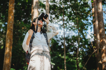 woman family walking in the forest to watching a bird in nature, using binocular for birding by looking on a tree, adventure travel activity in outdoor trekking lifestyle, searching wildlife in jungle