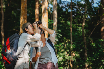 woman family walking in the forest to watching a bird in nature, using binocular for birding by looking on a tree, adventure travel activity in outdoor trekking lifestyle, searching wildlife in jungle
