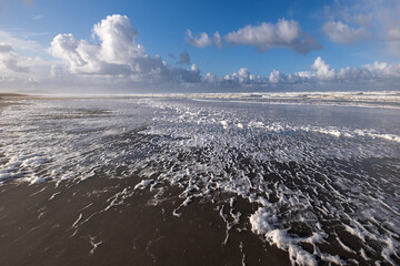 Long sandy beach with foamy waves and blue sky with beatutiful clouds. Long beach. Oregon. USA