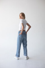 Beautiful blonde girl in a white T-shirt and blue jeans and sneakers posing on a white background