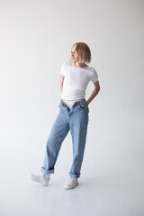 Beautiful blonde girl in a white T-shirt and blue jeans and sneakers posing on a white background