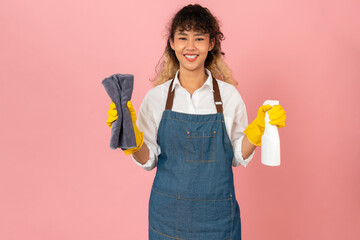 Attractive young Asian woman wearing apron with yellow rubber gloves and holding clean spray on...