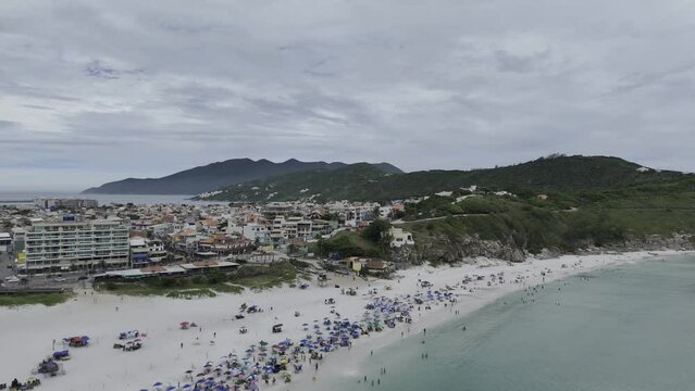 Drone flies up and over large white beach full of people