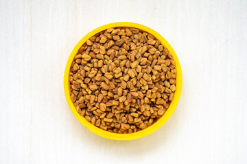 Organic dried fenugreek seeds on a yellow container on a white wooden background. Locally in Bangladesh, it is known as Methi Dana. 