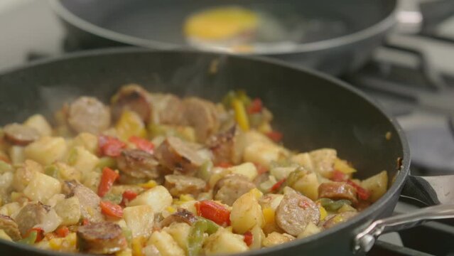 A breakfast hash of sausages, peppers, onions and potatoes simmers in a cast iron skillet.