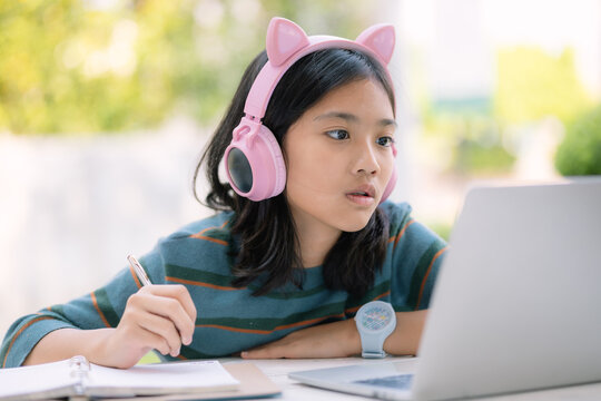 A girl wearing pink headphones is writing in a notebook - Powered by Adobe