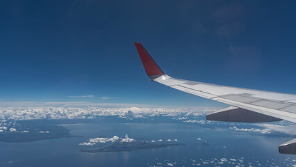 Obraz premium Tropical islands in the ocean are visible from the plane. White cumulus clouds over the sea. Reflection on calm water. The blue sky. In the foreground is an airplane wing. Malaysia