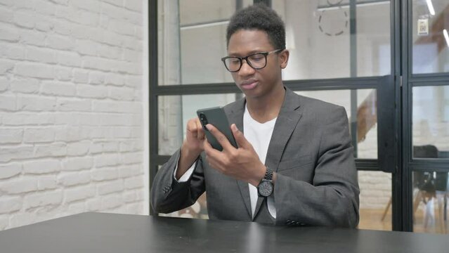 Young African Man Browsing Internet on Phone in Office