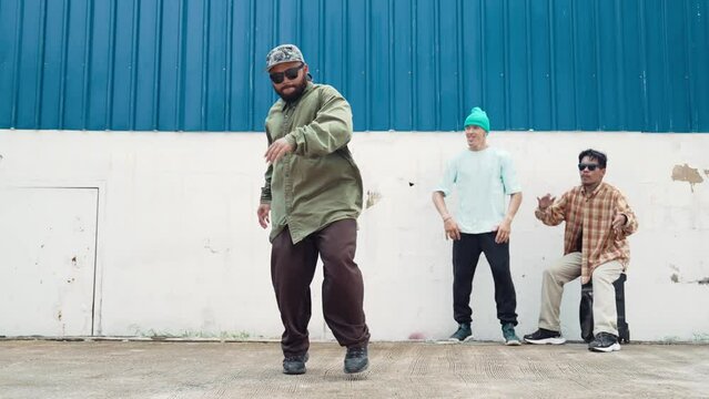 Skilled hipster doing cart wheel while multicultural friends encourage him. Hip-hop dancer moving foot step to music surrounded by group of hipster at wall near street. Outdoor sport 2024. hiphop.