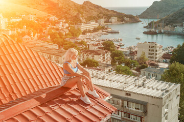 Woman sits on rooftop, enjoys town view and sea mountains. Peaceful rooftop relaxation. Below her,...