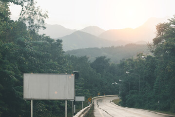An empty billboard stands by a winding road amidst foggy mountain scenery, signaling potential for...