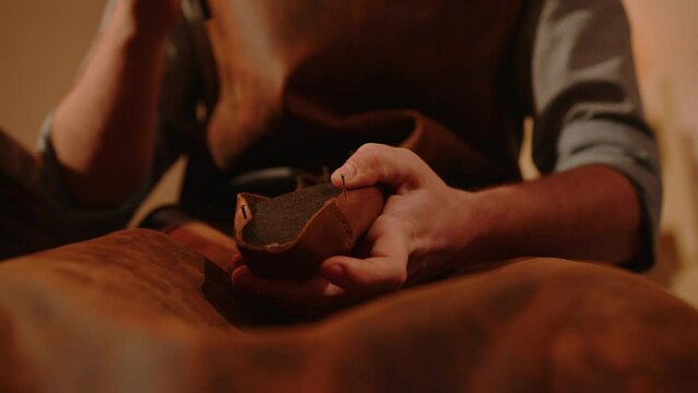 Shoemaker's hands stretching leather and nailing it with hammer to shoe last in shoe products tailoring studio. Craftsman in workshop making handmade shoes. 