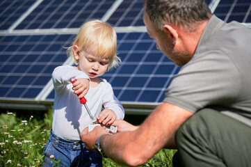 Dad showing to his little son how to use screwdriver in background of solar panels. Father teaching his child how to use tools. Son and his young dad learning tools.