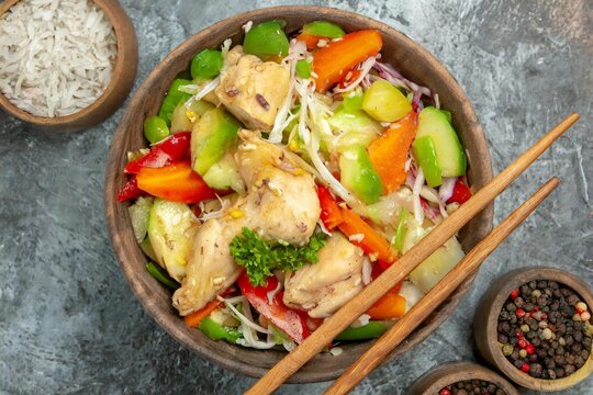 Top shot of a bowl of chicken vegetable salad with wooden chopsticks on top of a grey backround