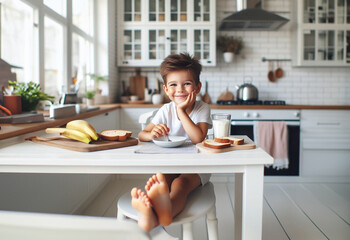 Junge Kind Heranwachsender sitzt fröhlich glücklich lächelnd barfuß am Tisch Frühstück zu Hause in hell Ausstattung Kindheit Ernährung Genuß Freude, Start in den Tag, Küche lebensstil frühstücken - obrazy, fototapety, plakaty