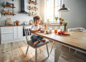 Junge Kind Heranwachsender sitzt fröhlich glücklich lächelnd barfuß am Tisch Frühstück zu Hause in hell Ausstattung Kindheit Ernährung Genuß Freude, Start in den Tag, Küche lebensstil frühstücken - obrazy, fototapety, plakaty