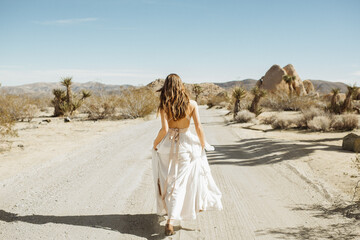Woman in a white boho wedding dress on a Joshua Tree desert road on a sunny day