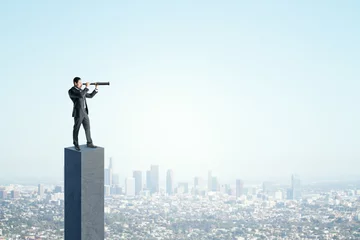 Foto auf Leinwand Side view of young businessman on concrete bar looking into the distance with telescope. Bright blue sky and city background. Strategy, forecast and goal concept. Mock up place for advertisement. © Who is Danny