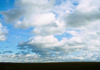 Grünes Ackerfeld vor großer blauer Himmellandschaft mit vielen weißen Wolken bei Sonne am...