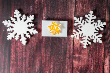 Snowflakes and a present with ribbon on a brown wooden background. Christmas winter flatlay with copyspace