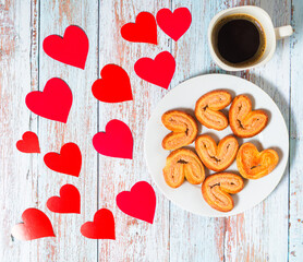 A cup of coffee, a plate with heart-shaped cookies on a wooden table. Background with copyspace for...