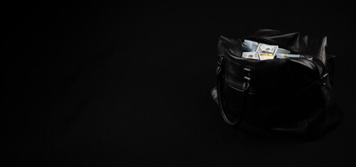 A bag with a lot of dollars money stands on a black background. Copy space. A large bag full of money on a black background next to an empty space for an inscription. Advertising.