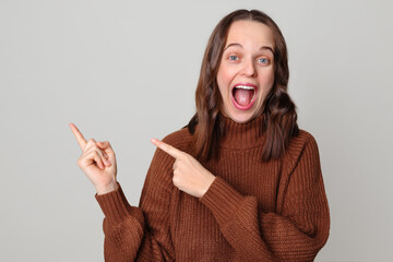 Excited overjoyed brown haired woman wearing brown jumper standing isolated over light gray...