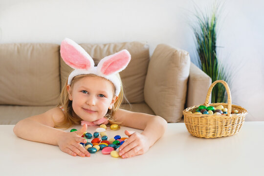 Blond child girl wearing bunny ears on Easter day play with Easter candys eggs at home