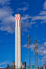 Concrete chimney of power plant with pylon of power line and blue cloudy sky background at Swiss City of Zürich on a spring day. Photo taken March 23rd, 2024, Zurich, Switzerland.