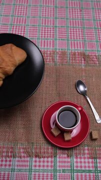 Persona mette in tavola il piatto con il croissant, video verticale, tazzina con caffè  